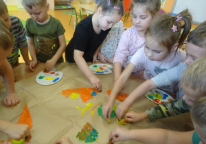 Ośmioro dzieci stempluje pomponami maczanymi w farbie sylwetę motyla.